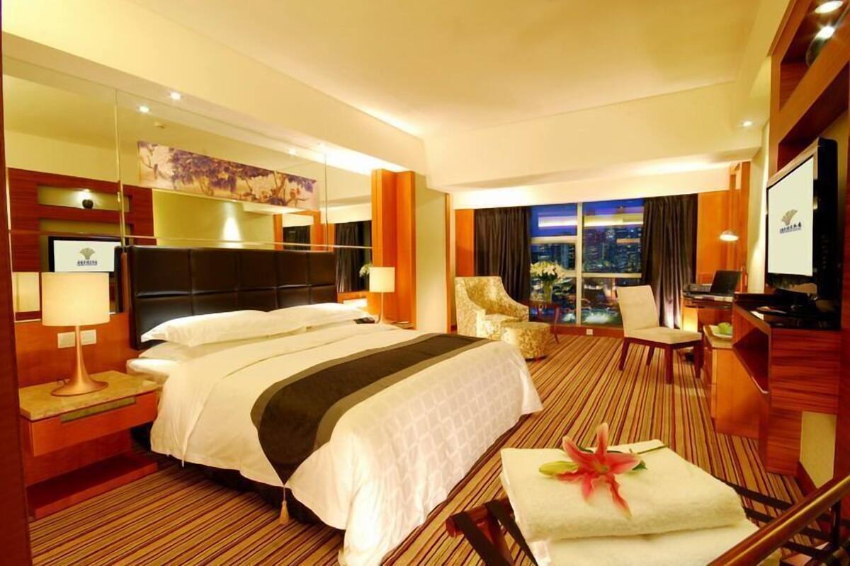 A hotel room with a large bed, a desk, a chair, a mirror, and a view of the city at night.