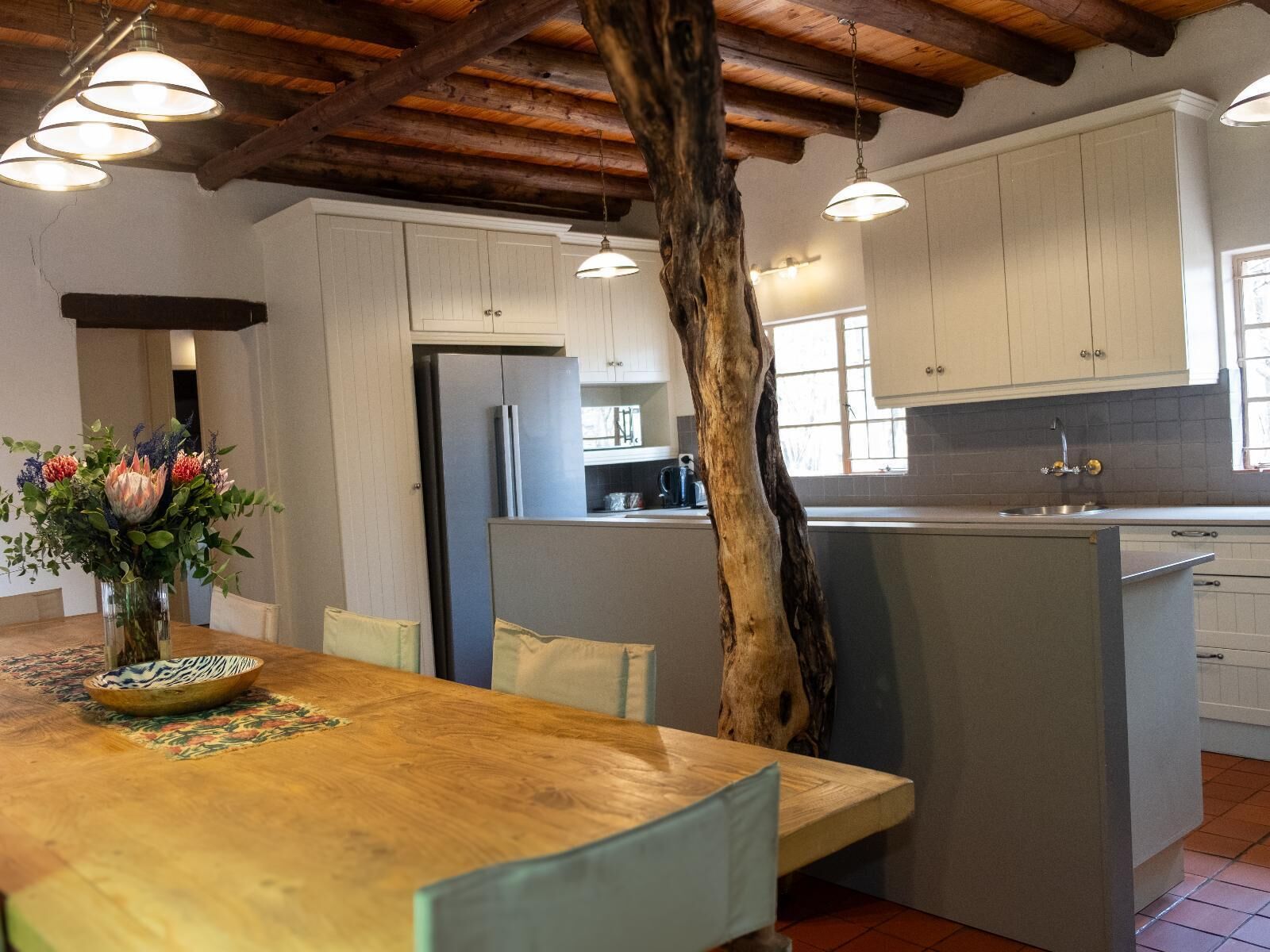 Una cocina con vigas de madera, armarios blancos, una isla central y un comedor con mesa y sillas de madera.