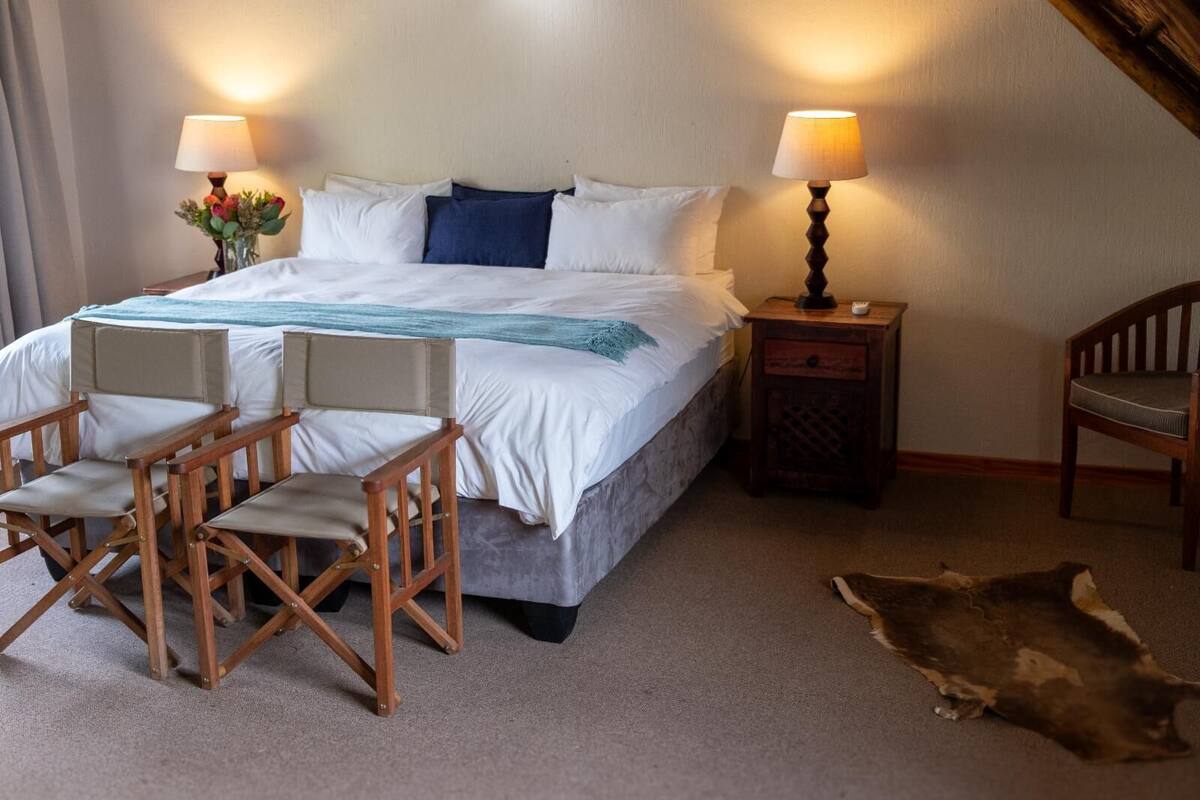 A neatly arranged bedroom with a large bed, two bedside tables with lamps, a chair, and a fur rug.
