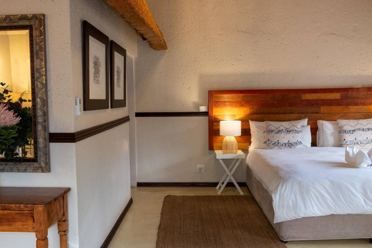 A bedroom with a wooden headboard, a bedside table with a lamp, a large bed with white bedding, and a framed picture on the wall.