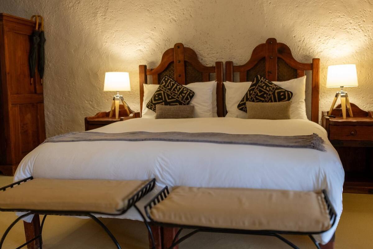 A neatly made bed with a wooden headboard, two bedside lamps, and a bench at the foot of the bed.