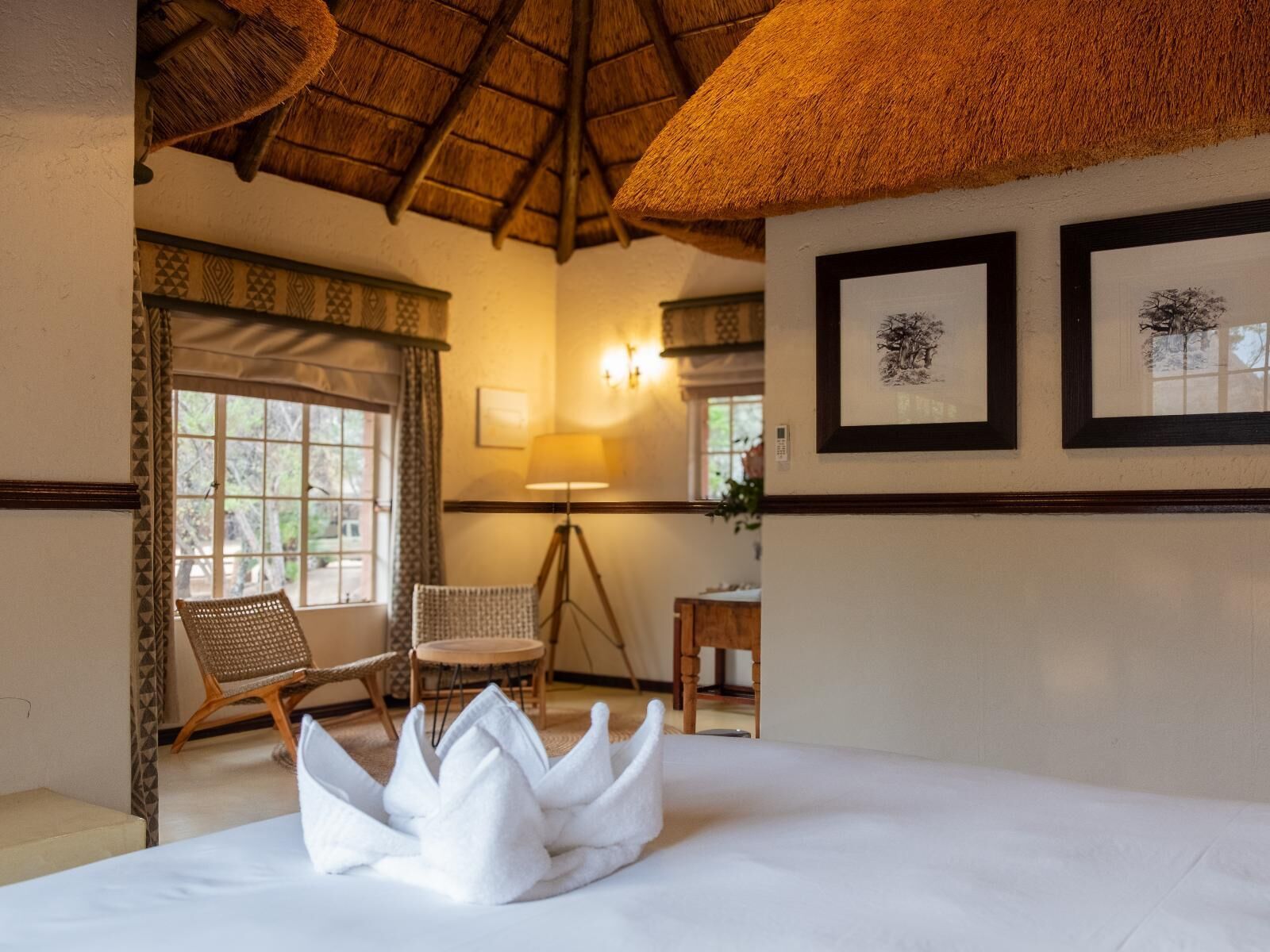 A hotel room with a bed, two wicker chairs, a lamp, and framed artwork on the wall.