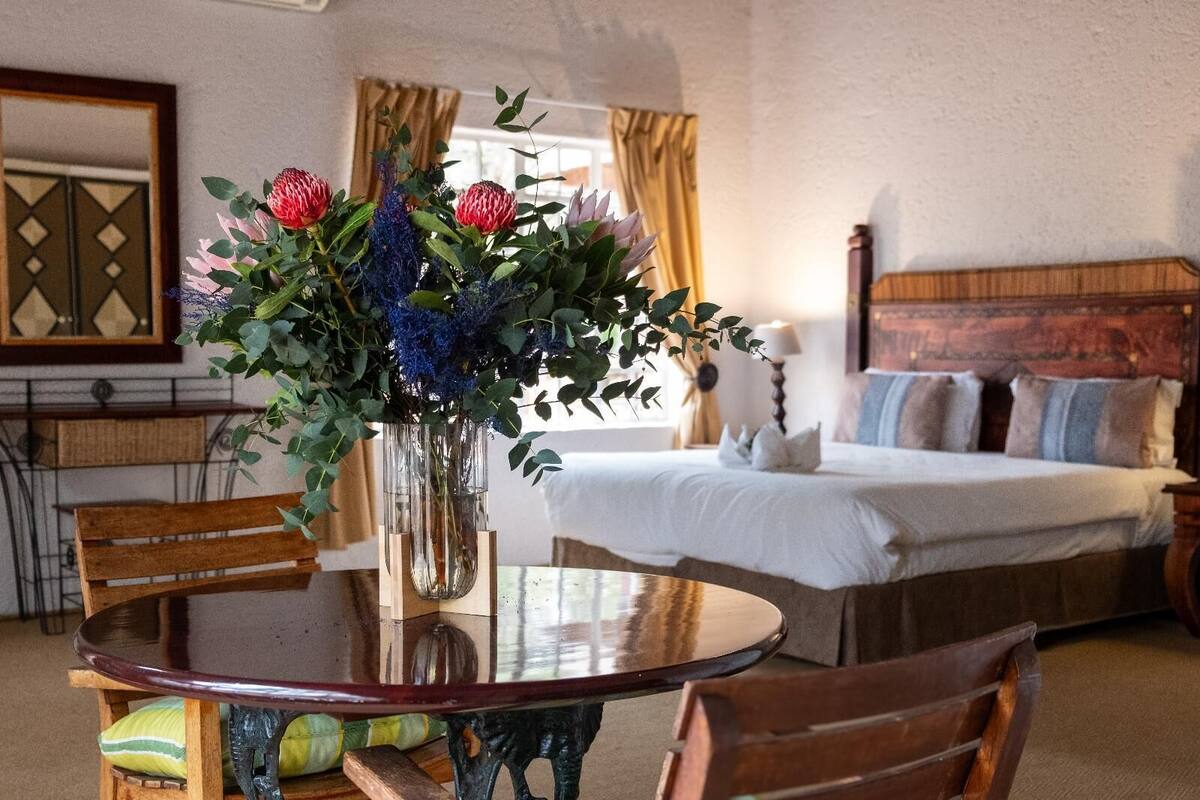 A hotel room with a bed, a round table with chairs, and a vase with flowers.