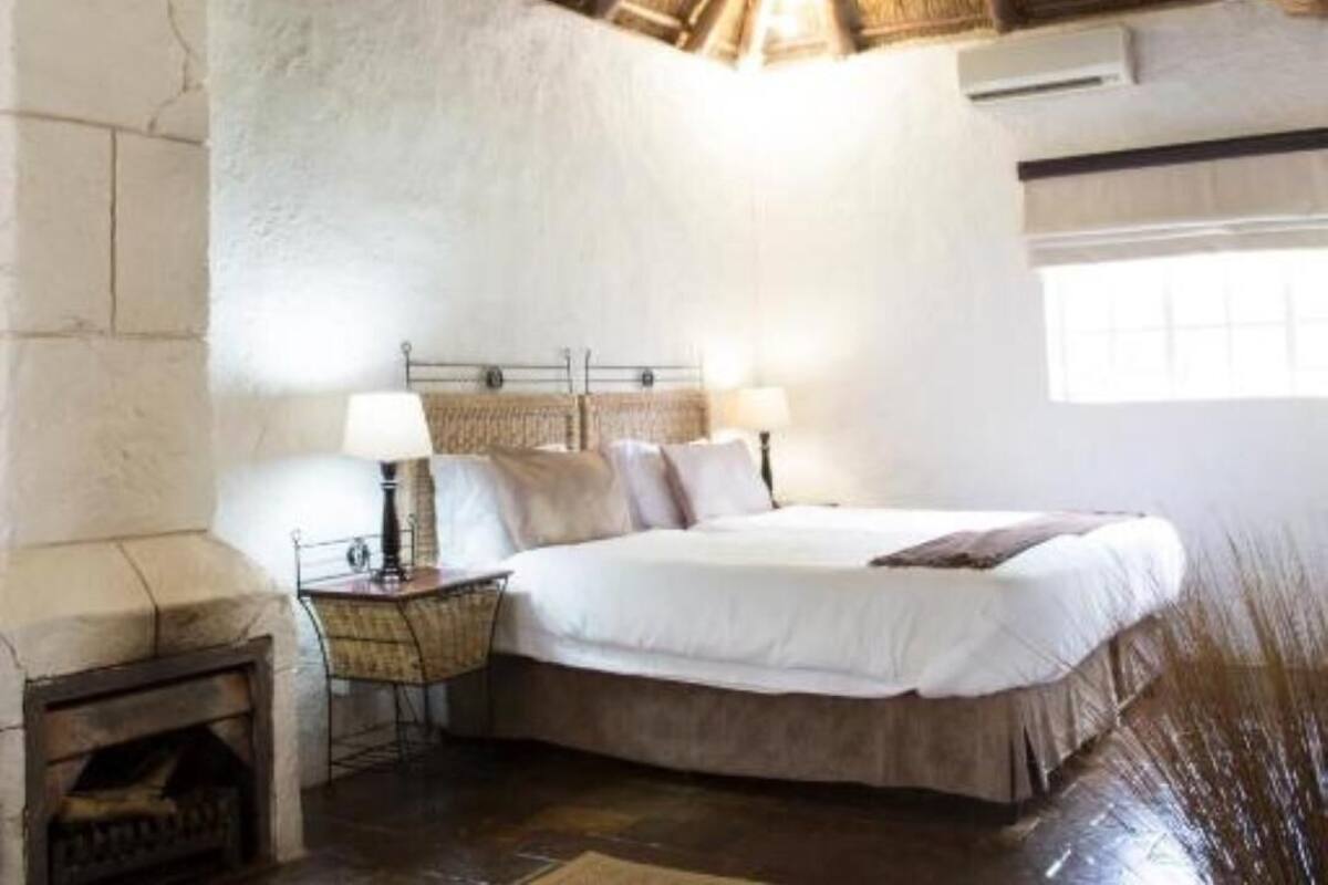 A bedroom with a large bed, a bedside table with a lamp, a fireplace, and a rustic ceiling.