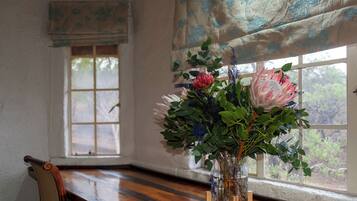 Una mesa de madera con un jarrón de flores frente a una ventana que da a árboles.