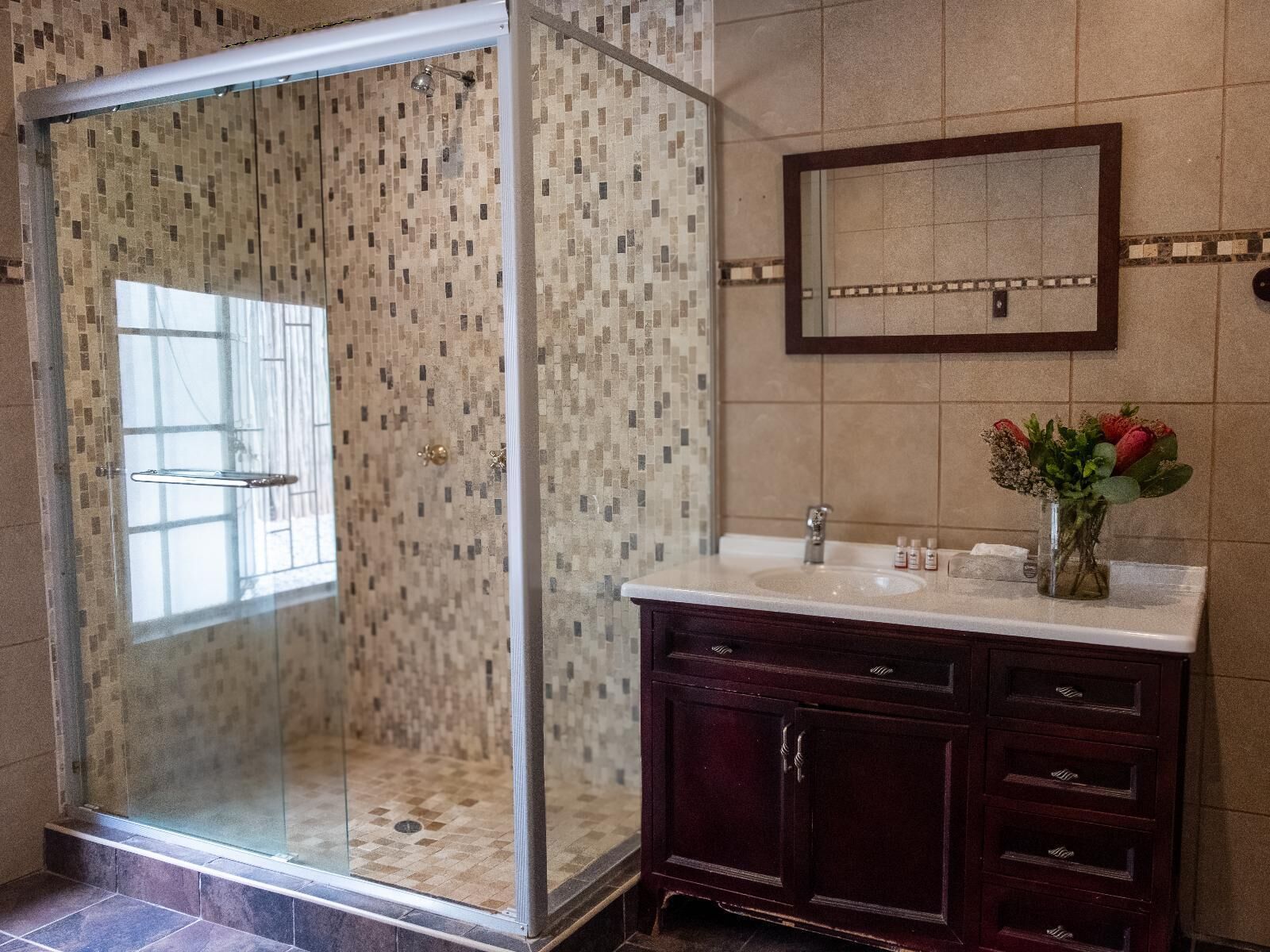 Un baño con ducha de vidrio, lavamanos de mármol y tocador de madera oscura.