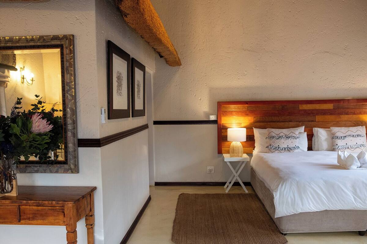 A bedroom with a wooden headboard, a bedside table with a lamp, a mirror, and framed pictures on the wall.