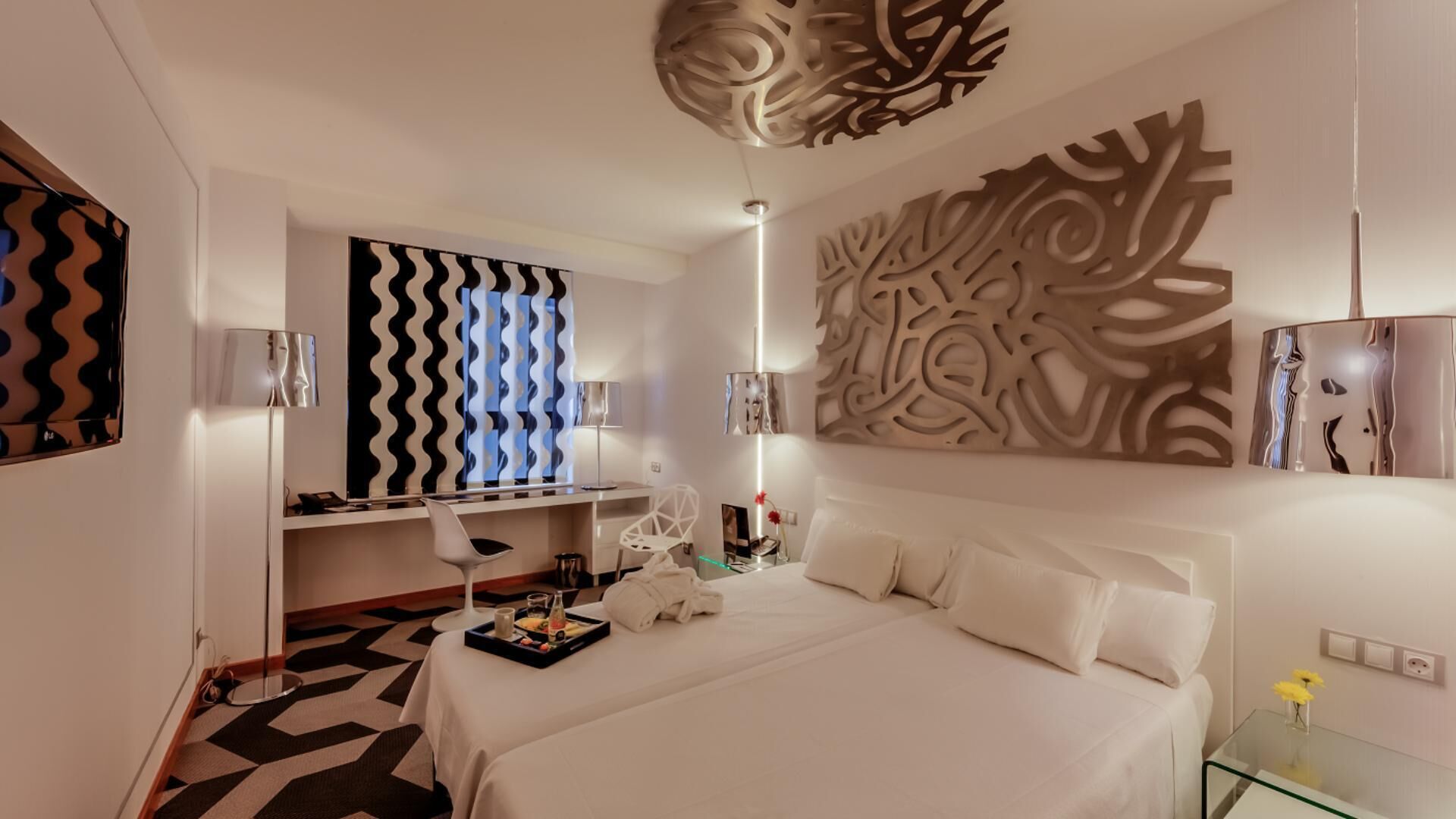 Een moderne hotelkamer met een net opgemaakt bed, een bureau met stoel, een decoratief paneel en een vloer met een patroon.