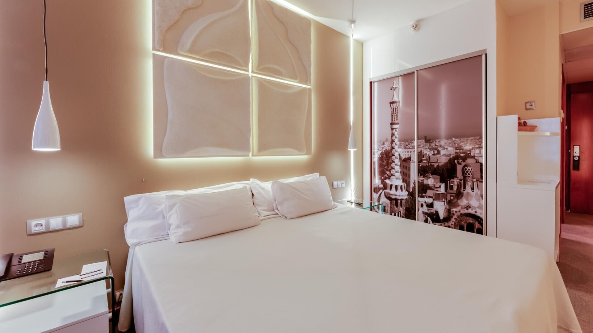 Habitación de hotel con una cama grande, teléfono en la mesita de noche y vistas a un paisaje urbano a través de la ventana.