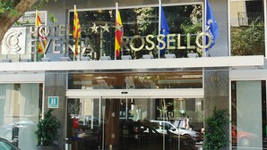 The exterior of Hotel Rossetto with a glass entrance, flags, and a parking area. - Evenia Rossello (Barcelona)