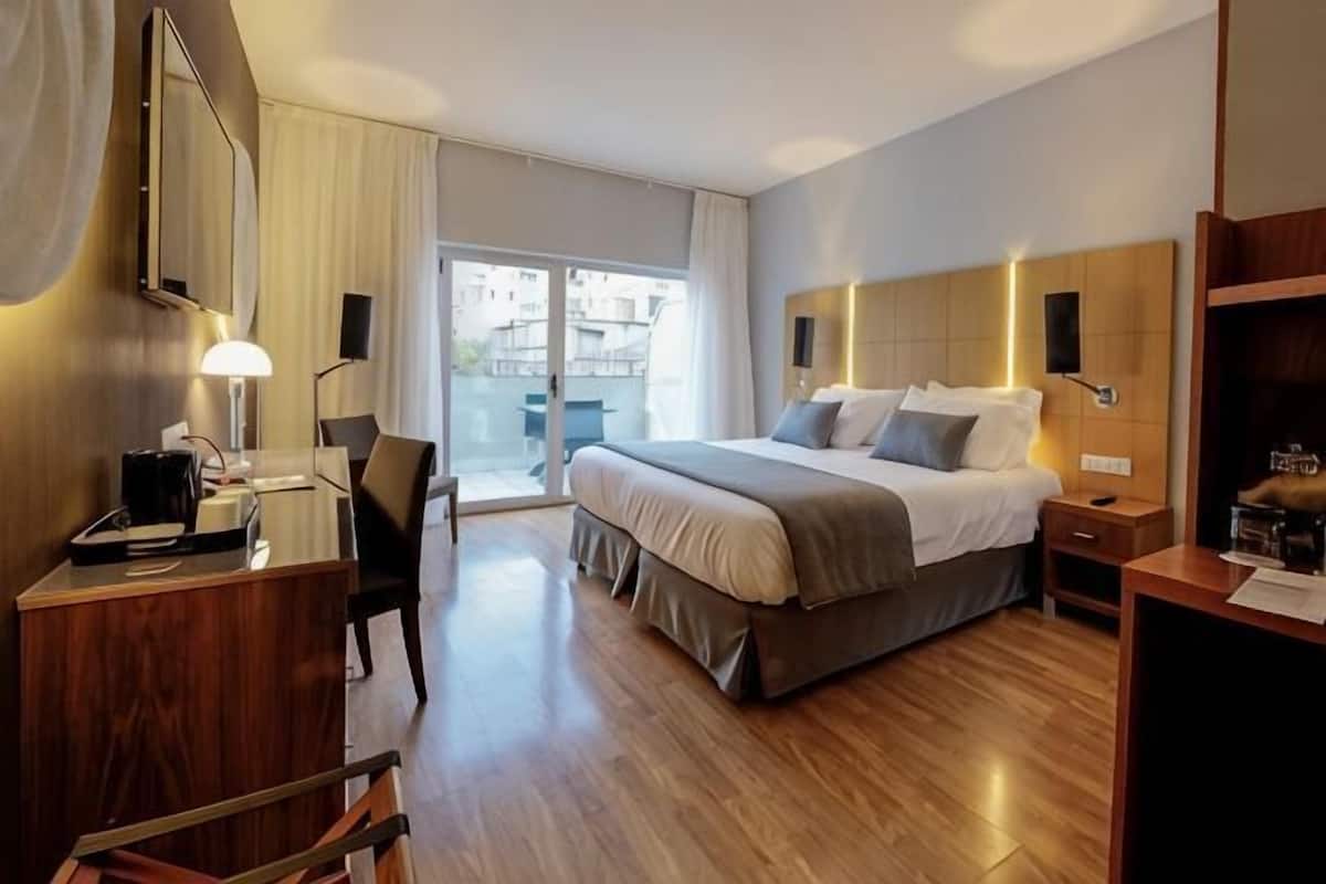 A hotel room with a bed, desk, chair, and a view of the outside.