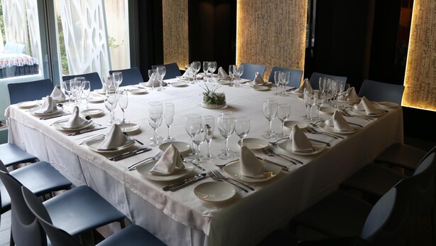 A long dining table set for a formal meal with white tablecloths, glassware, and neatly folded napkins. - Evenia Rossello (Barcelona)