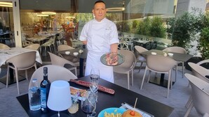 A chef standing at a table with a plate of food, wine glasses, and bottles of water. - Evenia Rossello (Barcelona)