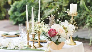 Ein Tisch, gedeckt mit einer weißen Tischdecke, goldenen Kerzenständern und einer Blumenarrangements.