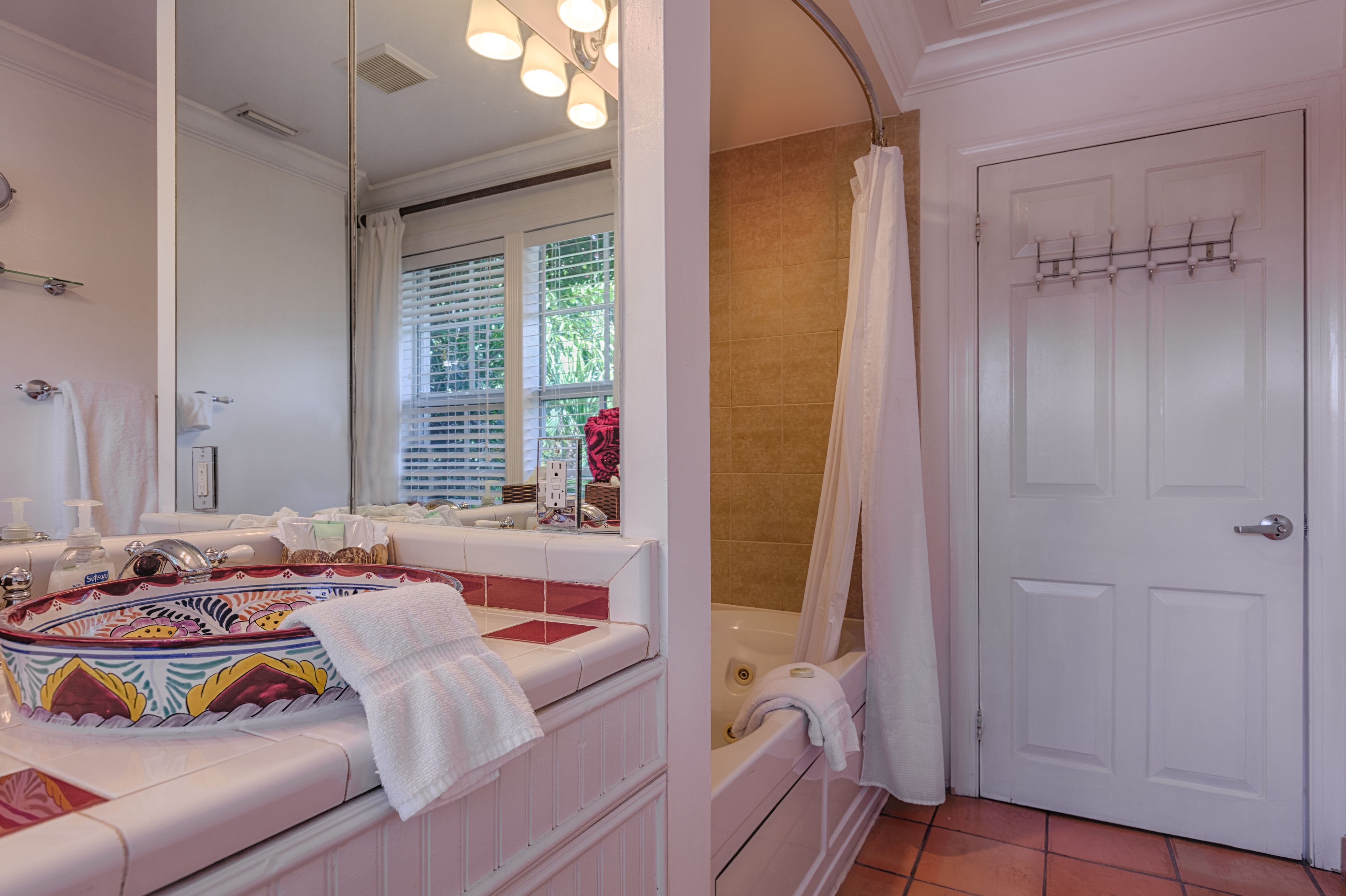 Une salle de bain avec un grand miroir, une baignoire, un rideau de douche et une porte blanche dotée d’un porte-serviettes.