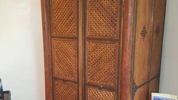 Een houten kast met een deur van geweven materiaal, een metalen standaard met een bordje, en een betegelde vloer.