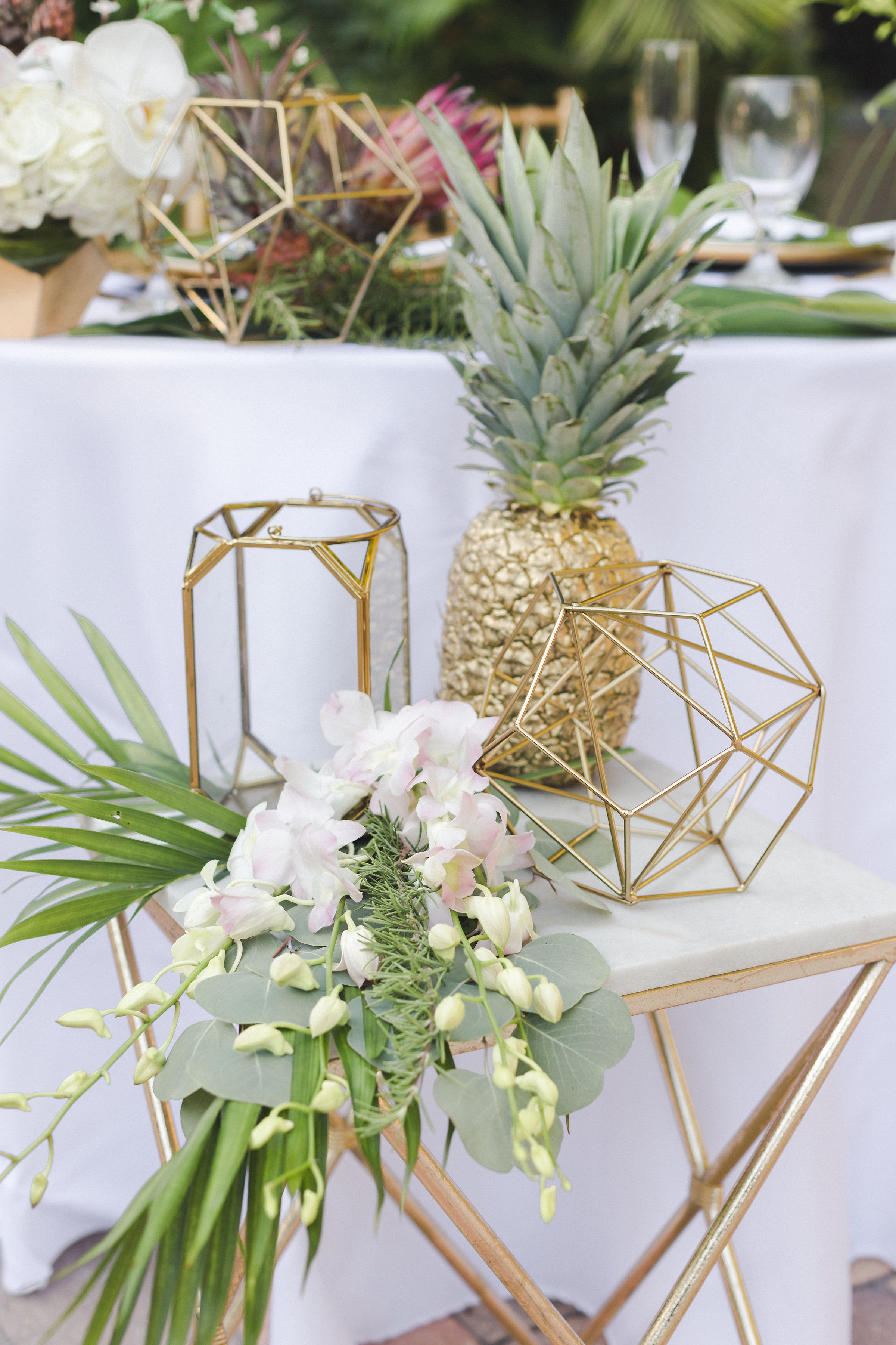 A table with a pineapple centerpiece, gold geometric candle holders, and a floral arrangement.
