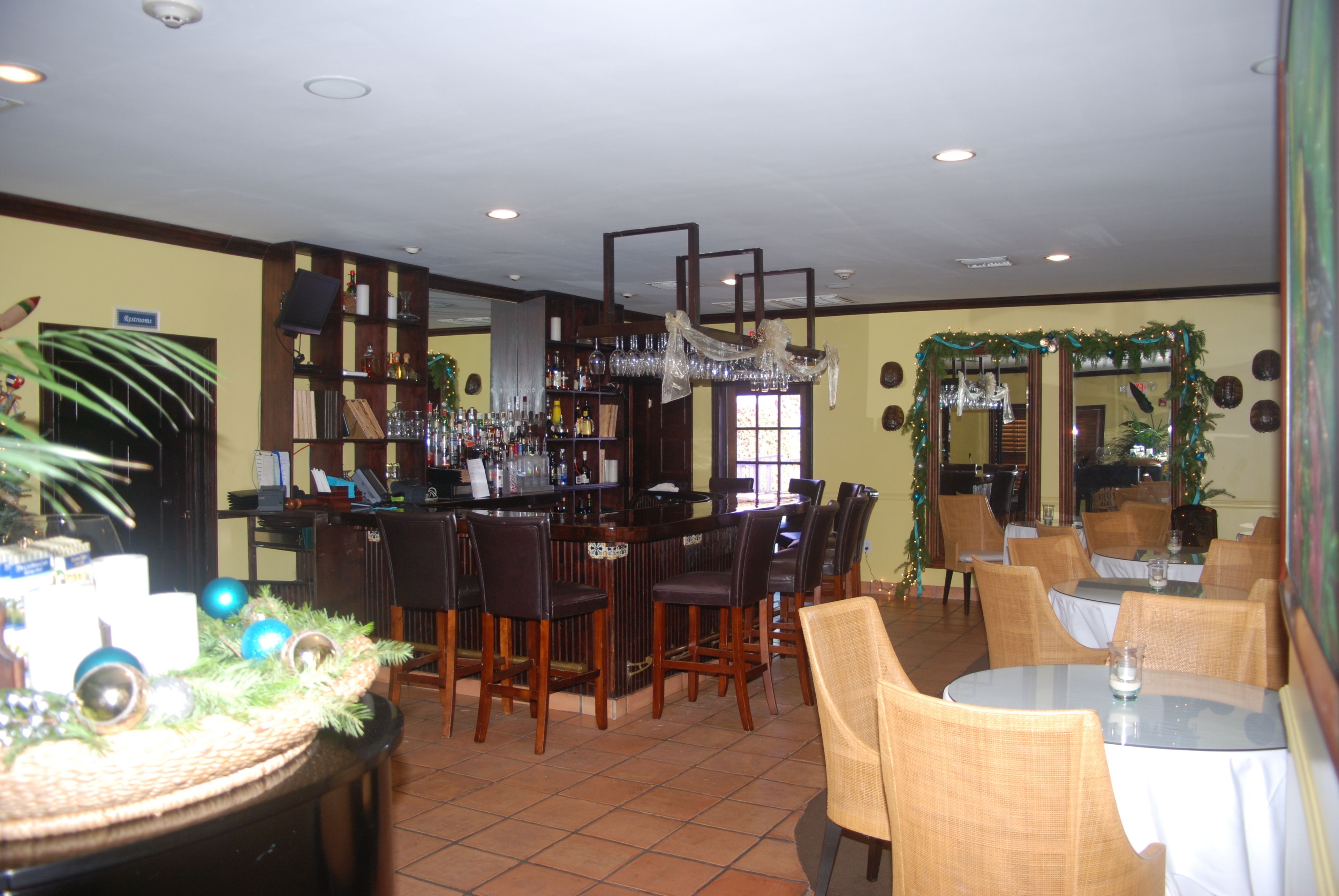 A bar area with wooden chairs and tables, a bar counter with bottles and glasses, and a Christmas tree decoration.