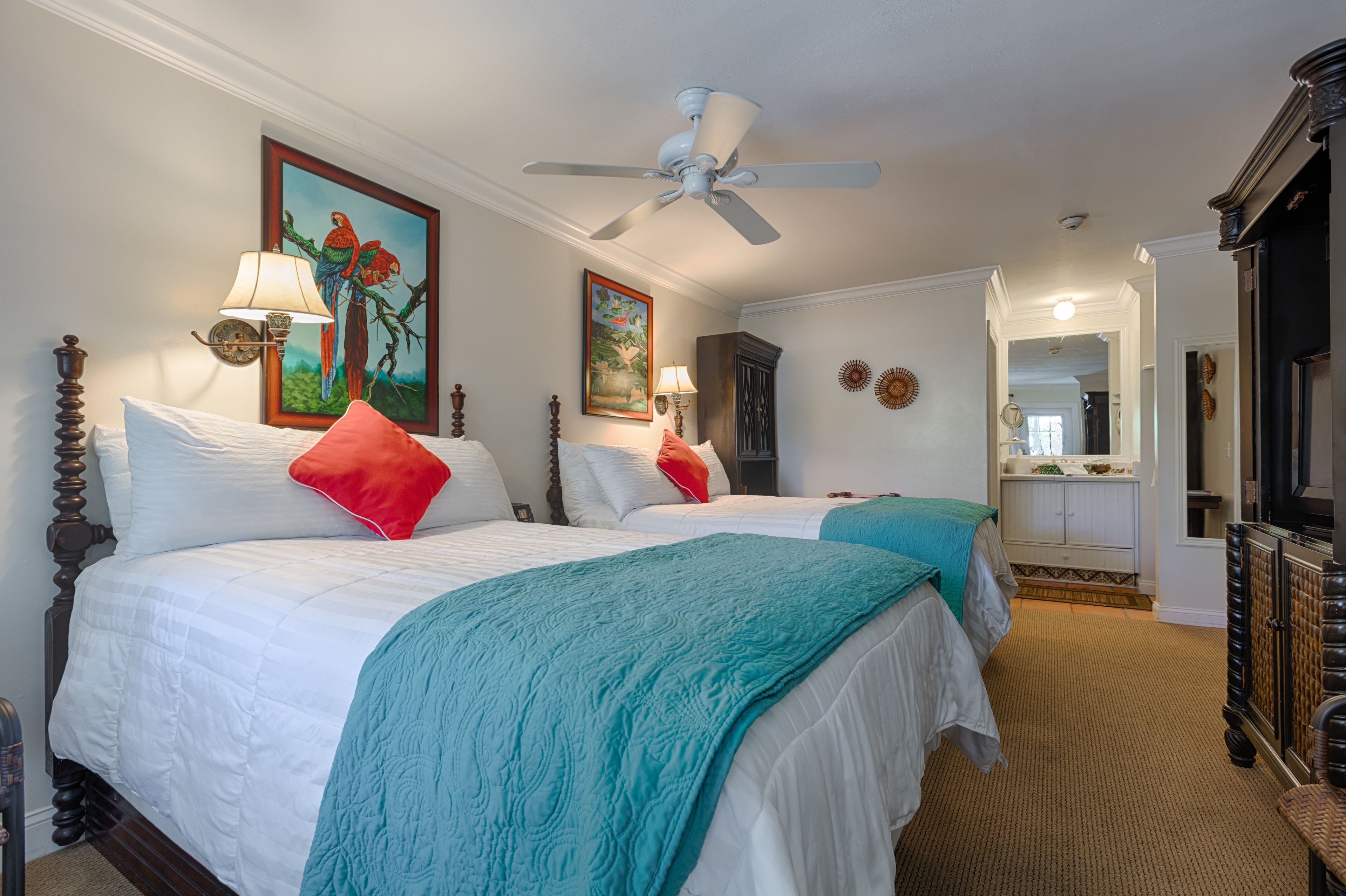 A hotel room with two beds, a ceiling fan, a large mirror, and a view of the hallway.