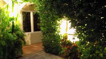 A pathway leading through a garden area with dense foliage and a building entrance.