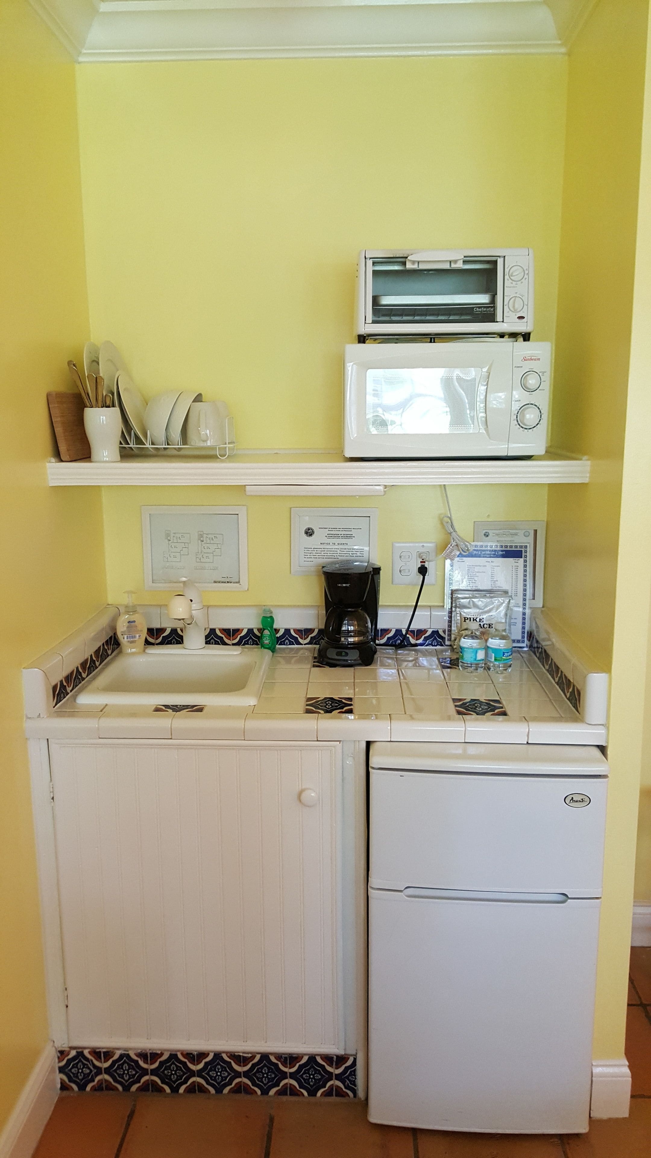 Eine kompakte Küche mit Mikrowelle, Kaffeemaschine und einem kleinen Kühlschrank.