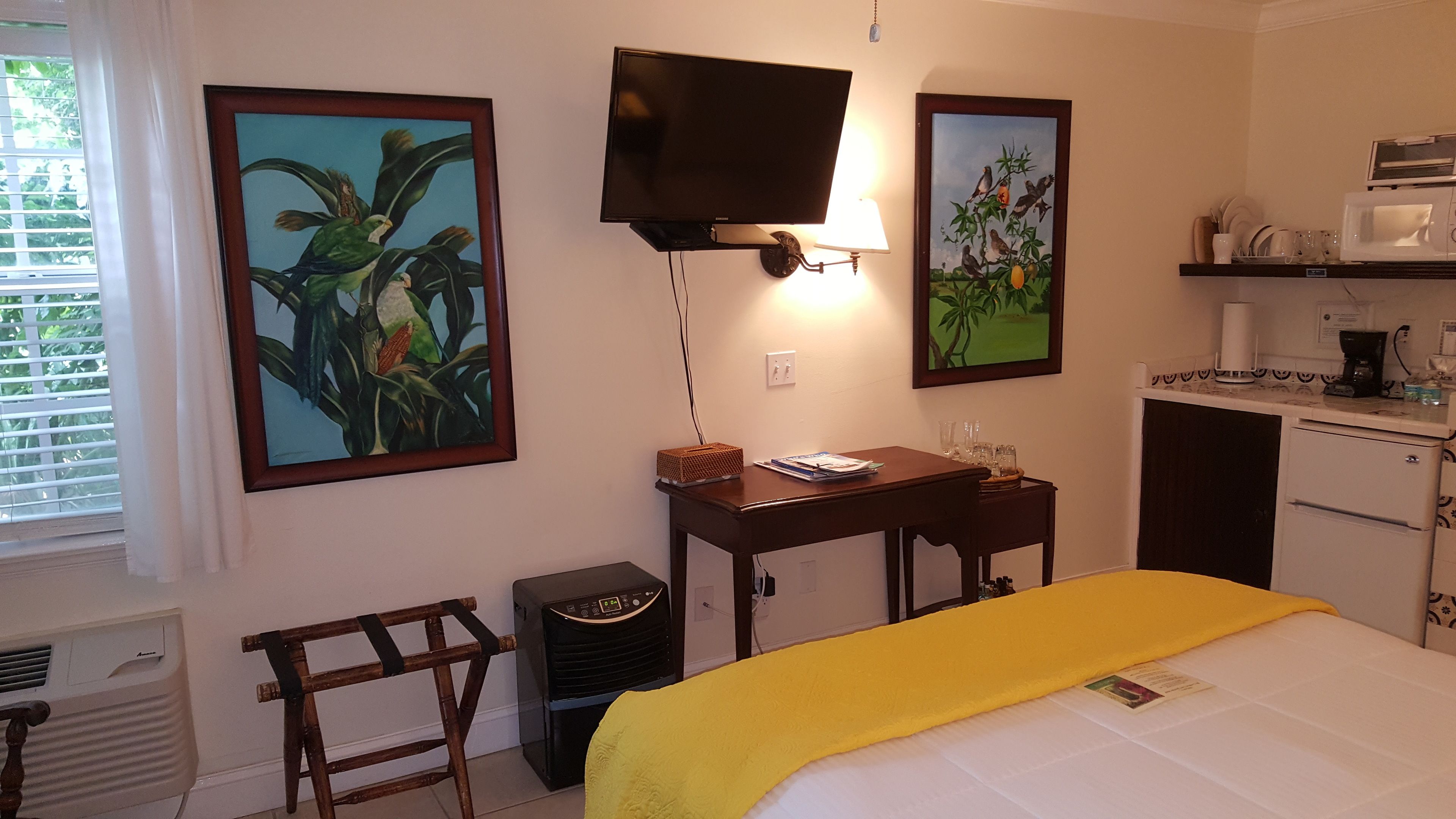 A hotel room with a bed, a desk with a lamp, a television, and artwork on the walls.