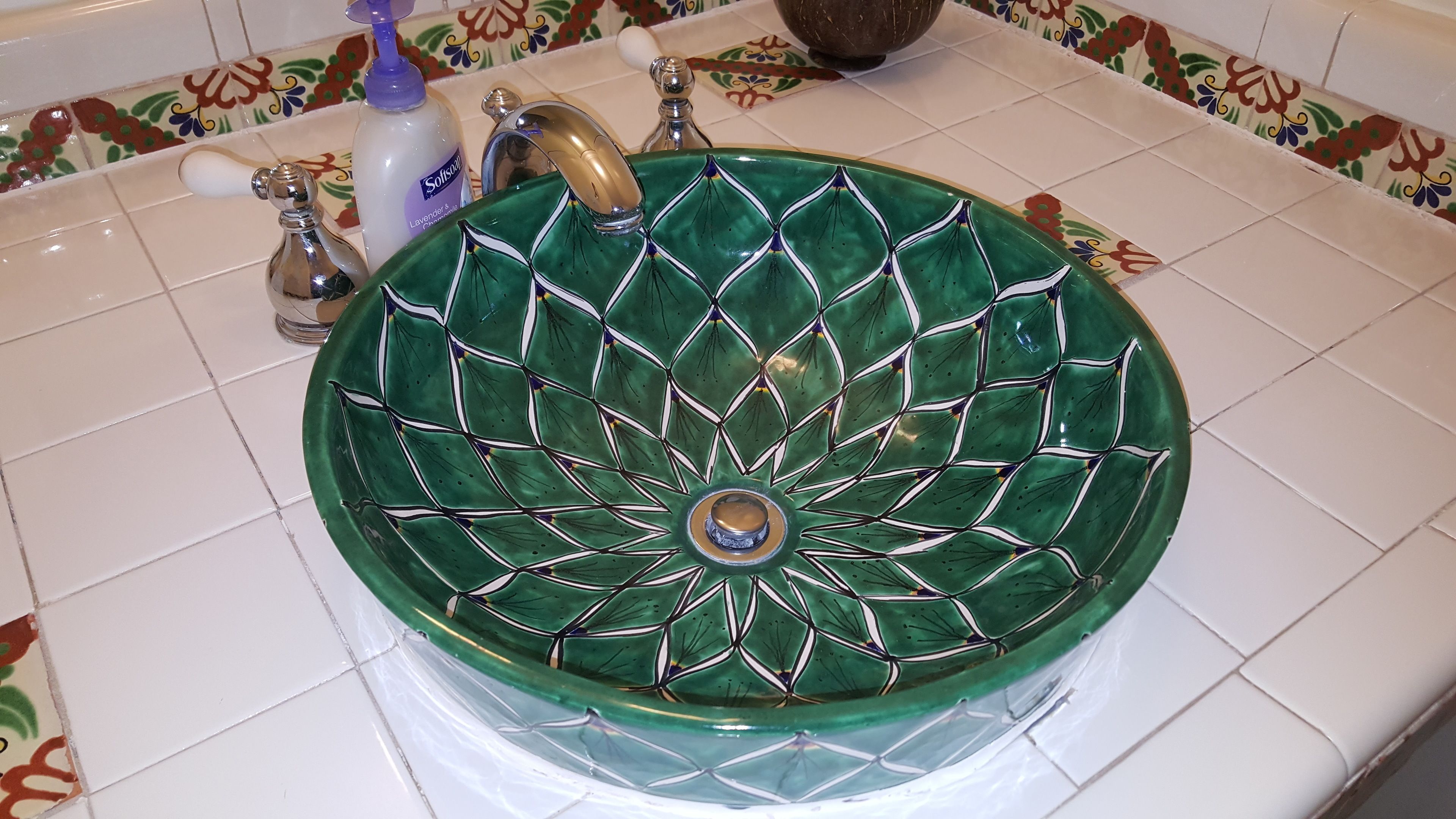 Un évier en céramique verte orné d’un motif géométrique, avec un robinet et un distributeur de savon.
