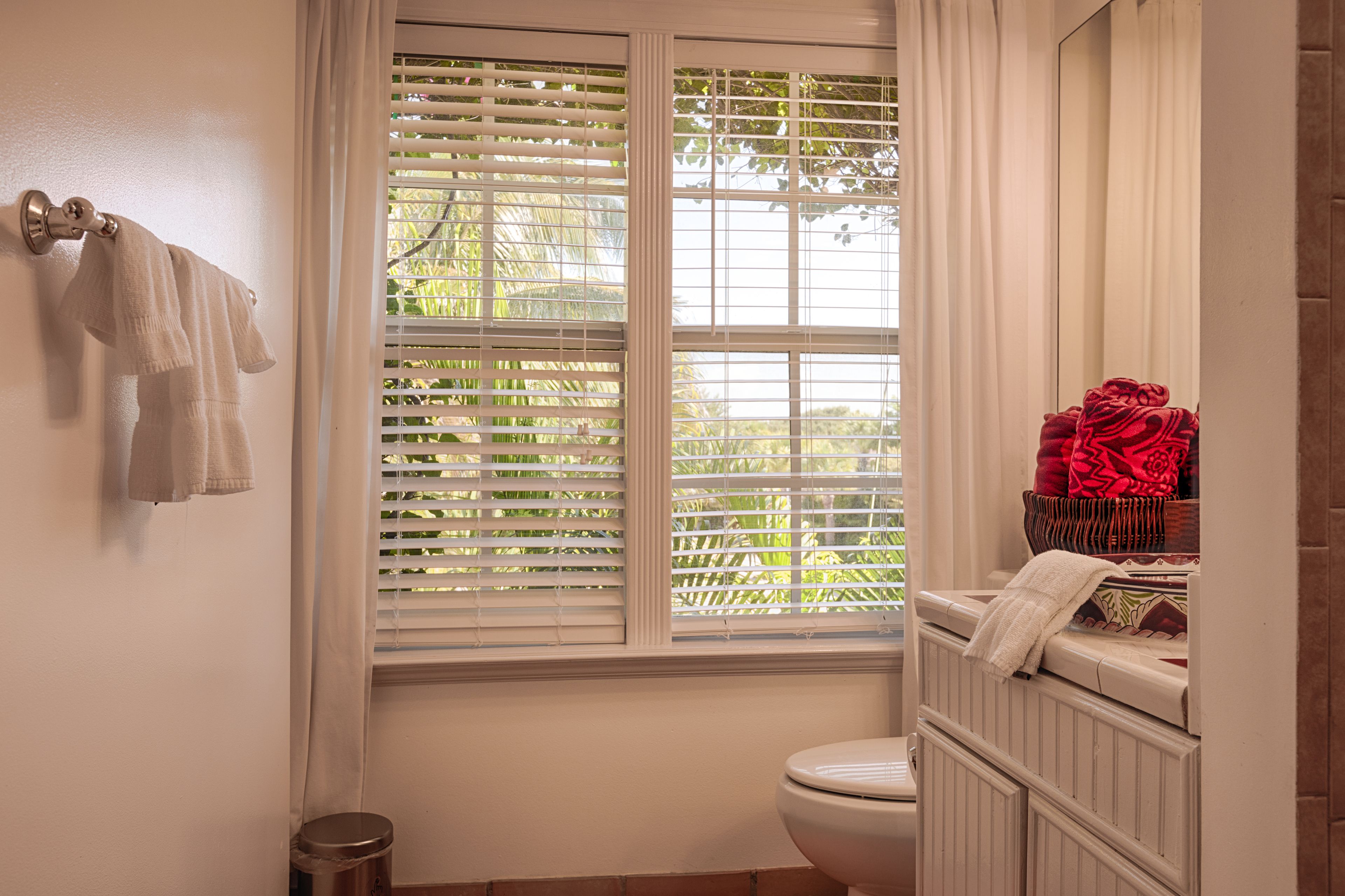 A bathroom with a toilet, a window with blinds, and a towel rack with towels.