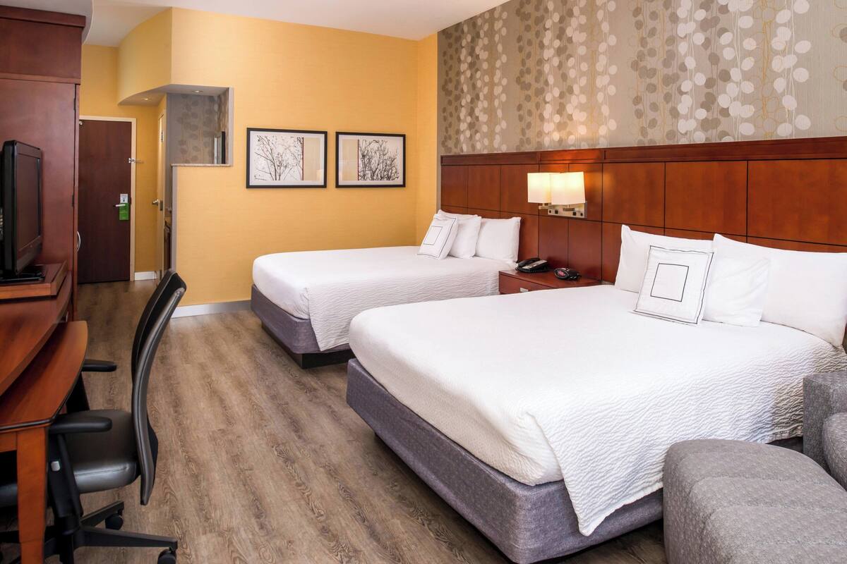 A hotel room with two beds, a desk, a chair, and a television.