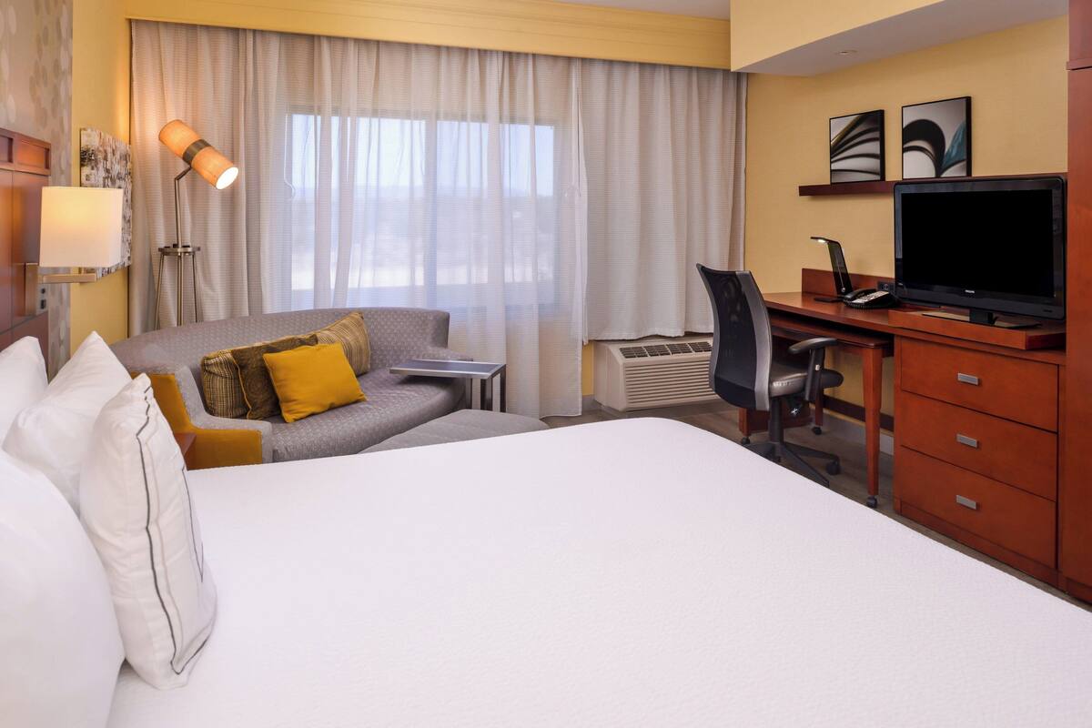 A hotel room with a large bed, a desk with a computer, a chair, and a television.