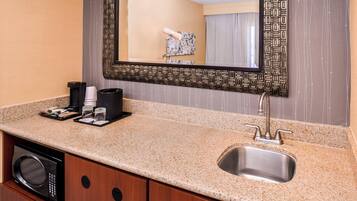 A hotel bathroom with a granite countertop, a sink, a mirror, and a built-in washing machine.