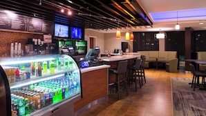 A bar area with a refrigerated display case, bar stools, and a counter with a cash register.