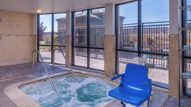 A hot tub with a blue chair, a ladder, and a view of a pool and buildings outside.
