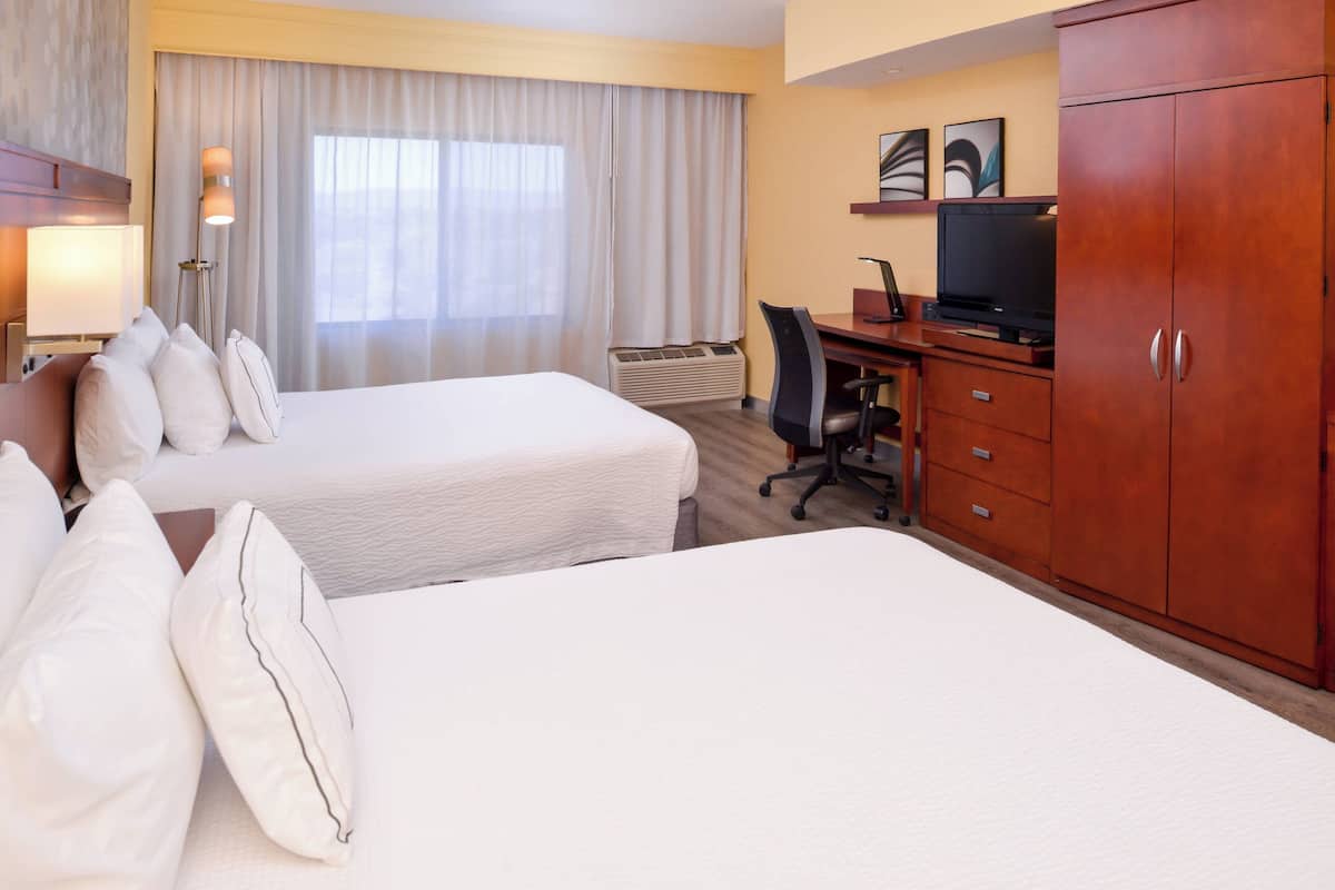 A hotel room with two beds, a desk, a television, and a wardrobe.