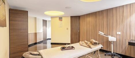 A modern room with a massage table, wooden panel walls, and a ceiling light fixture.