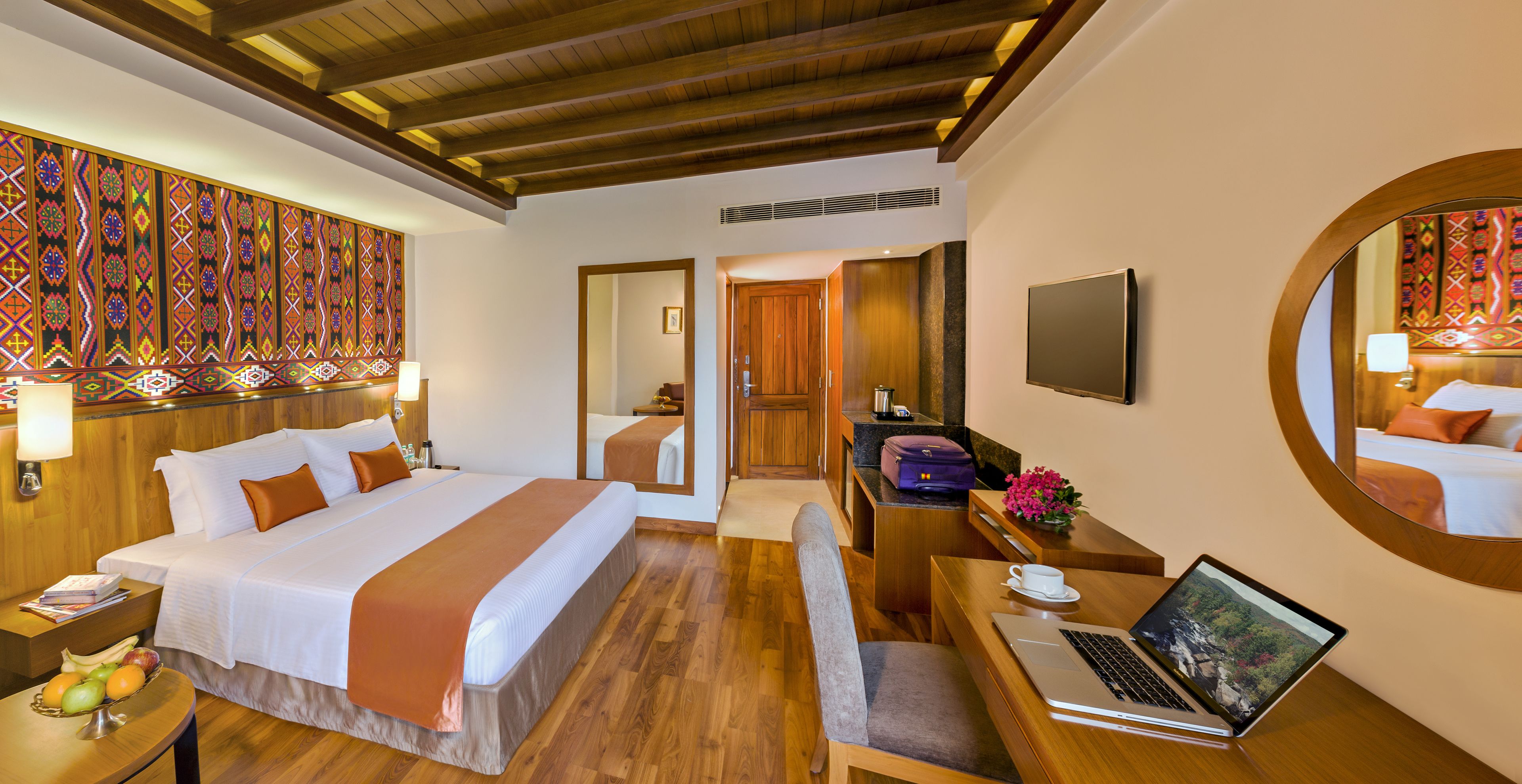 A hotel room with a large bed, a desk with a laptop, a chair, and a small table with fruit.