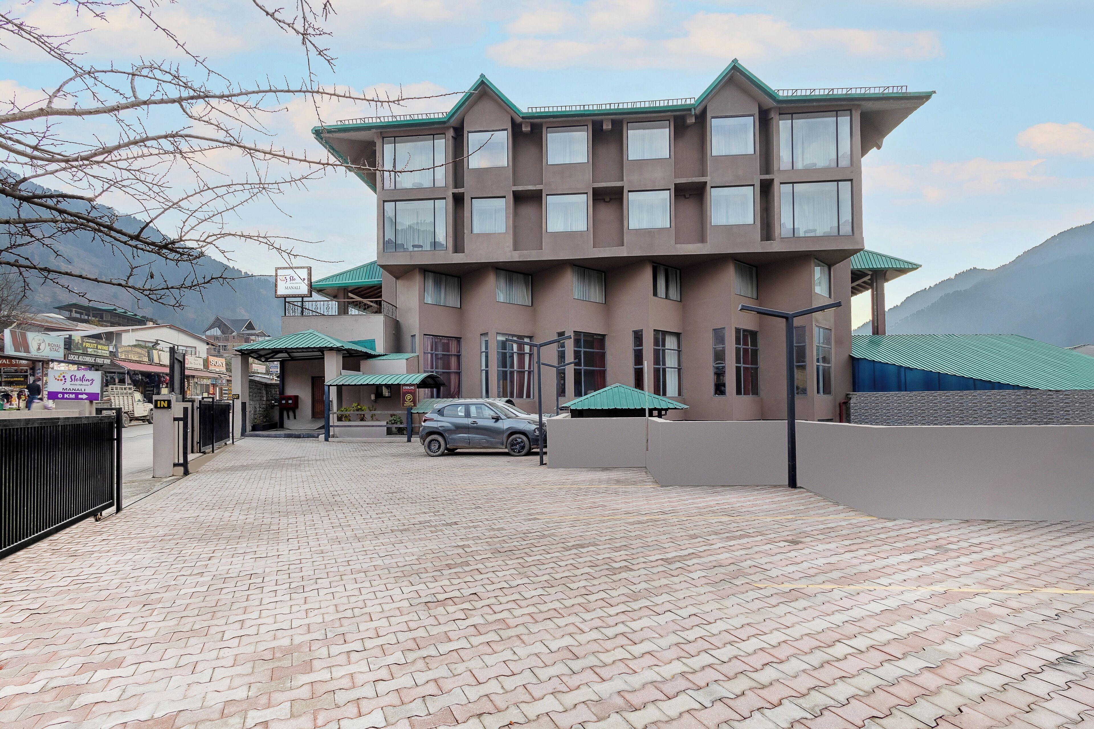 Un edificio de varios pisos con diseño moderno, que presenta una entrada con adoquines de ladrillo y un coche estacionado al frente.