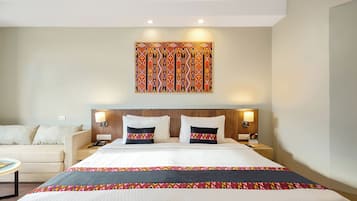 Une chambre d’hôtel avec un grand lit, deux tables de chevet, une petite table, une lampe et une œuvre d’art accrochée au mur.