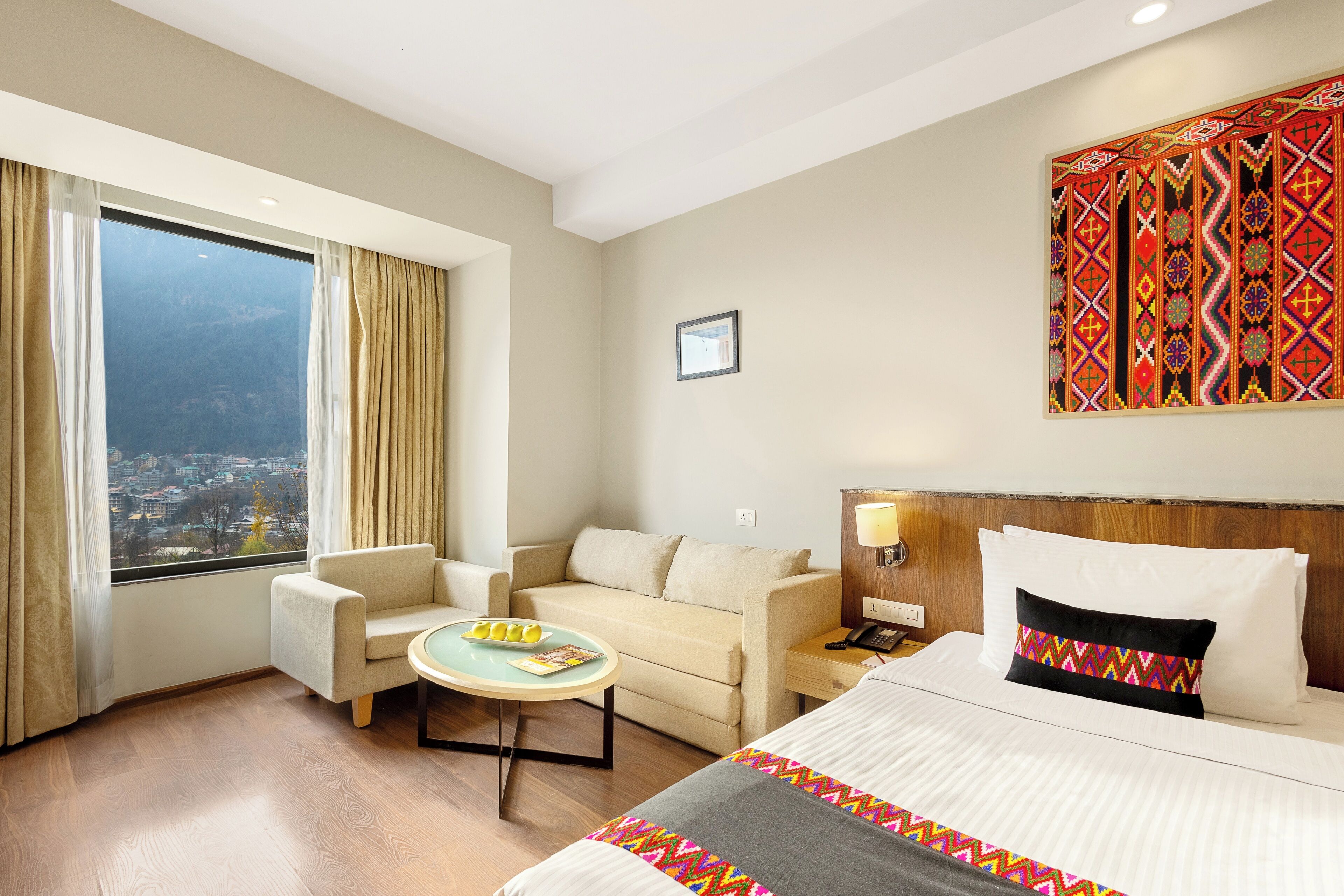 A hotel room with a bed, a sofa, a small table, and a window with curtains.
