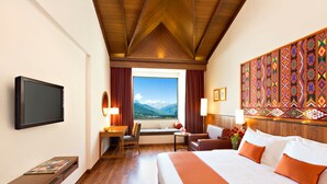 Ein Hotelzimmer mit einem großen Bett, einem Schreibtisch mit Stuhl, einem Fernseher und einem Fenster mit Bergblick.