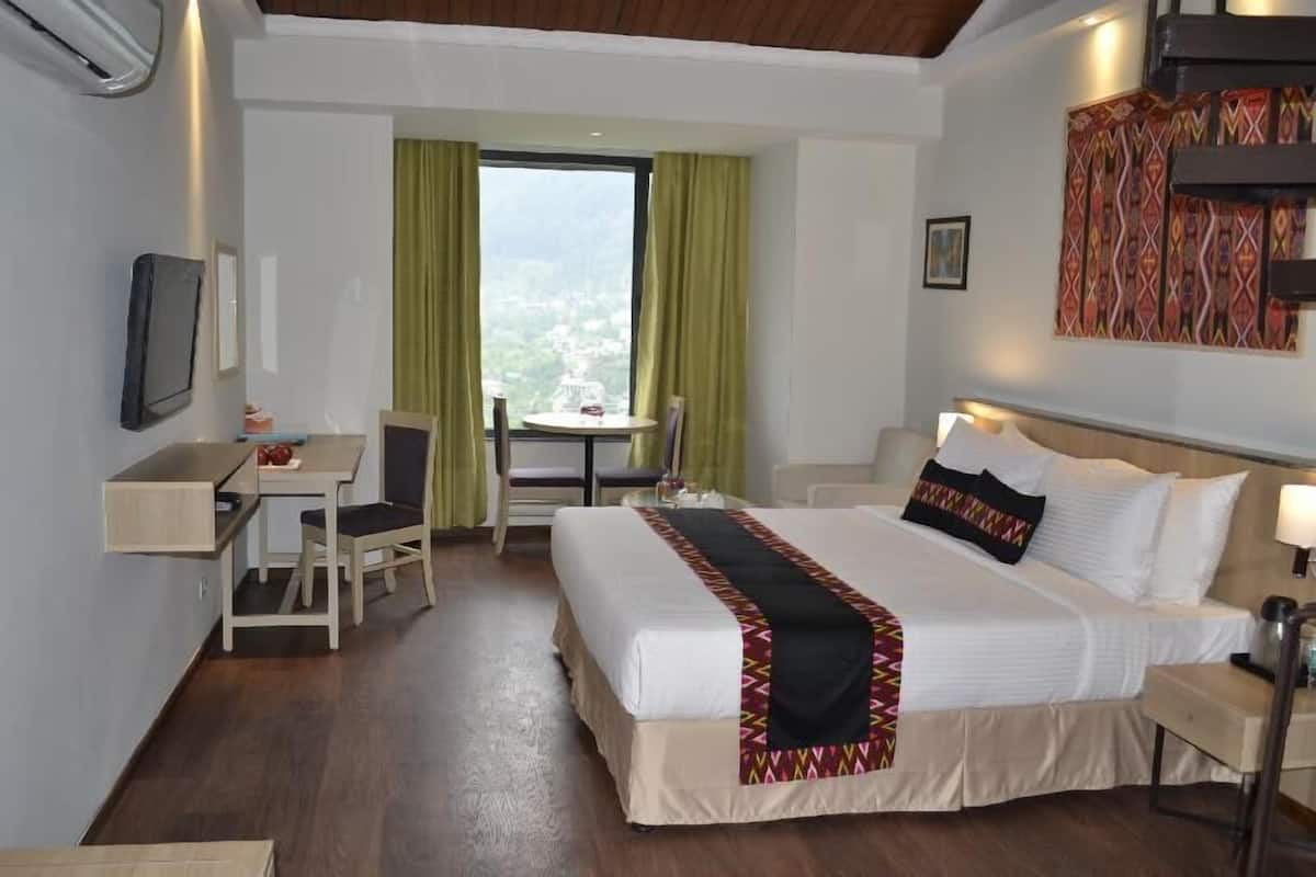 Ein Hotelzimmer mit Bett, Schreibtisch, Stuhl, einem kleinen Tisch und einem Fenster mit Vorhängen.