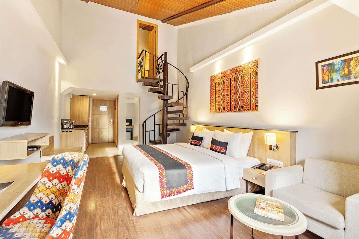 Ein Hotelzimmer mit Bett, Schlafsofa, Fernseher, Schreibtisch, Stuhl, Nachttisch, Lampe, einem Gemälde und einer Treppe.