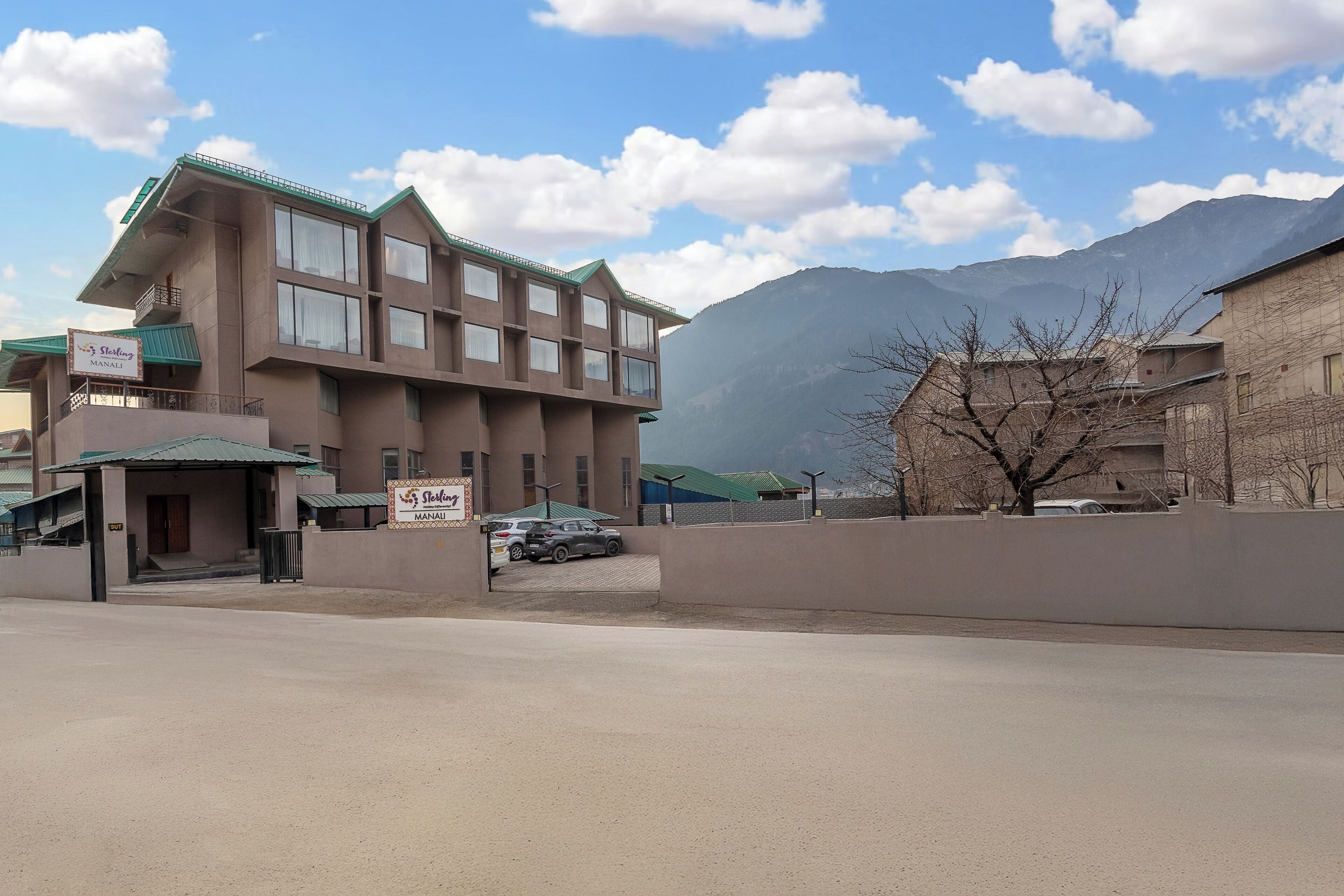 A hotel with a signboard, a parking area, and a mountain backdrop.