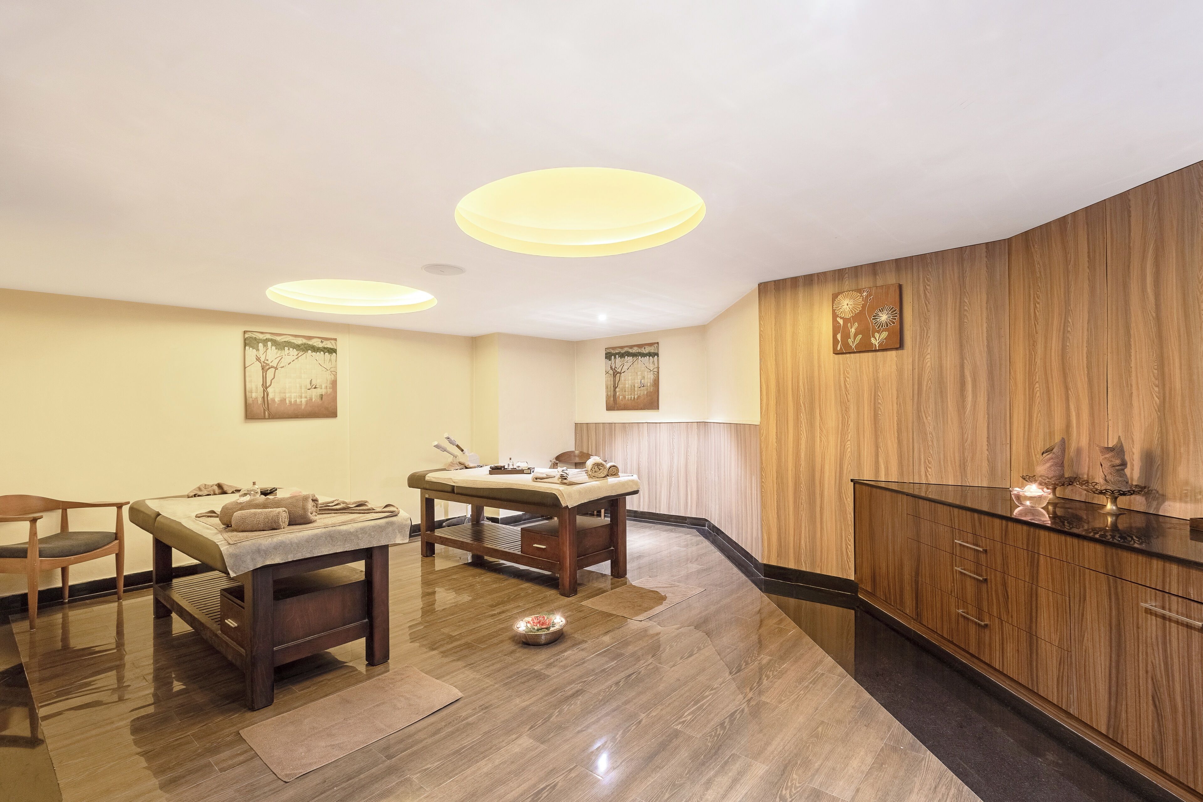 Moderni spa-huone, jossa on hierontapöytä, puukaapit ja taideteoksia seinillä.
