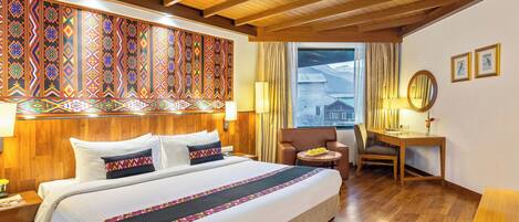 Ett hotellrum med en stor säng, ett träpanelat tak, ett skrivbord och utsikt över bergen genom fönstret.