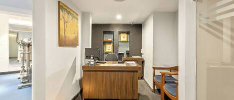 A reception desk with a wooden finish, a painting above it, and a small plate with food and a candle on the floor.