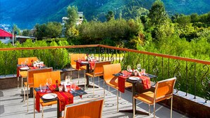 Eine Terrasse im Freien mit Tischen und Stühlen, vor einer Bergkulisse und wolkenlosem Himmel.