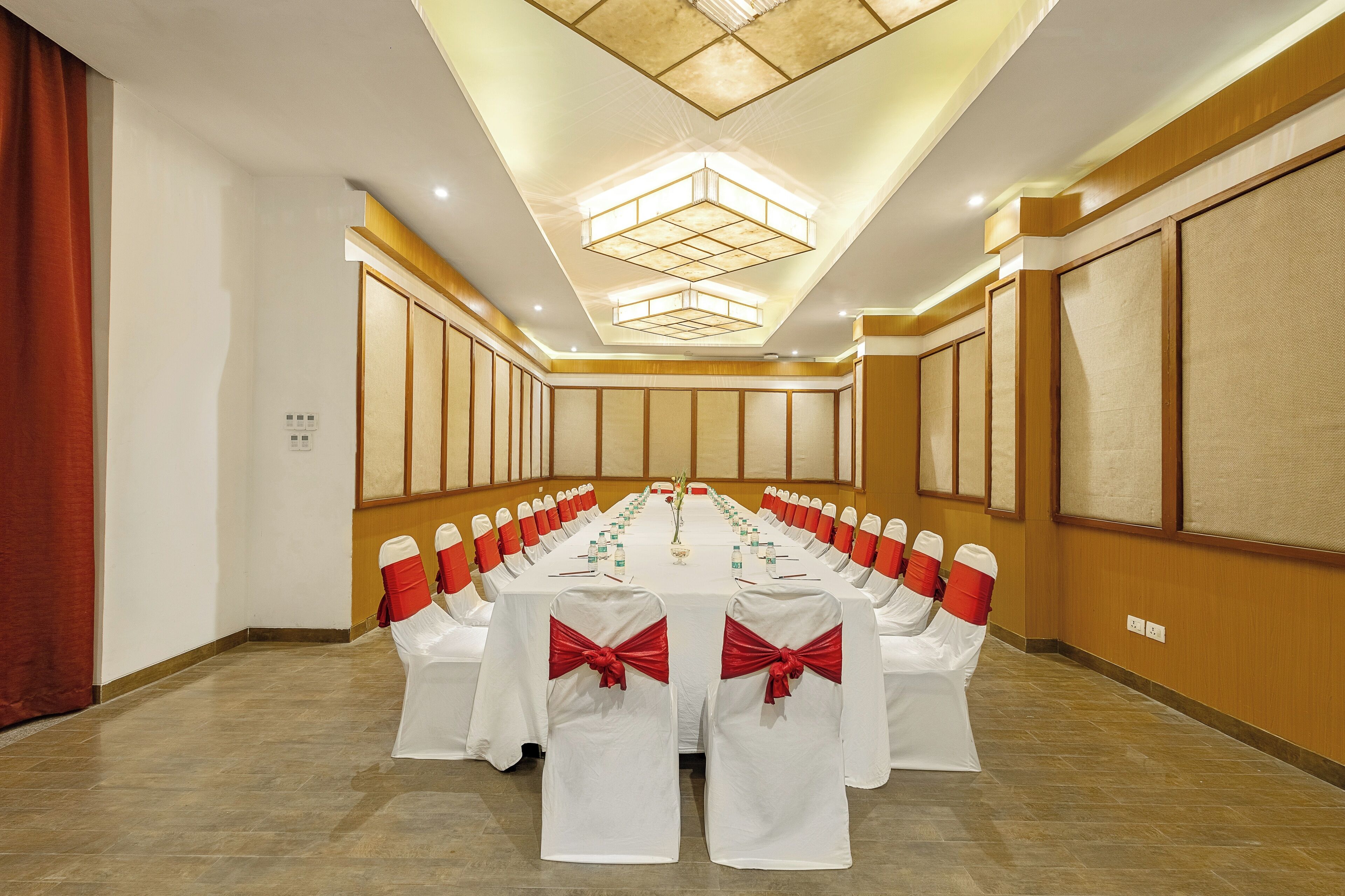 A conference room with a long table, white chairs with red sashes, and a modern ceiling design.