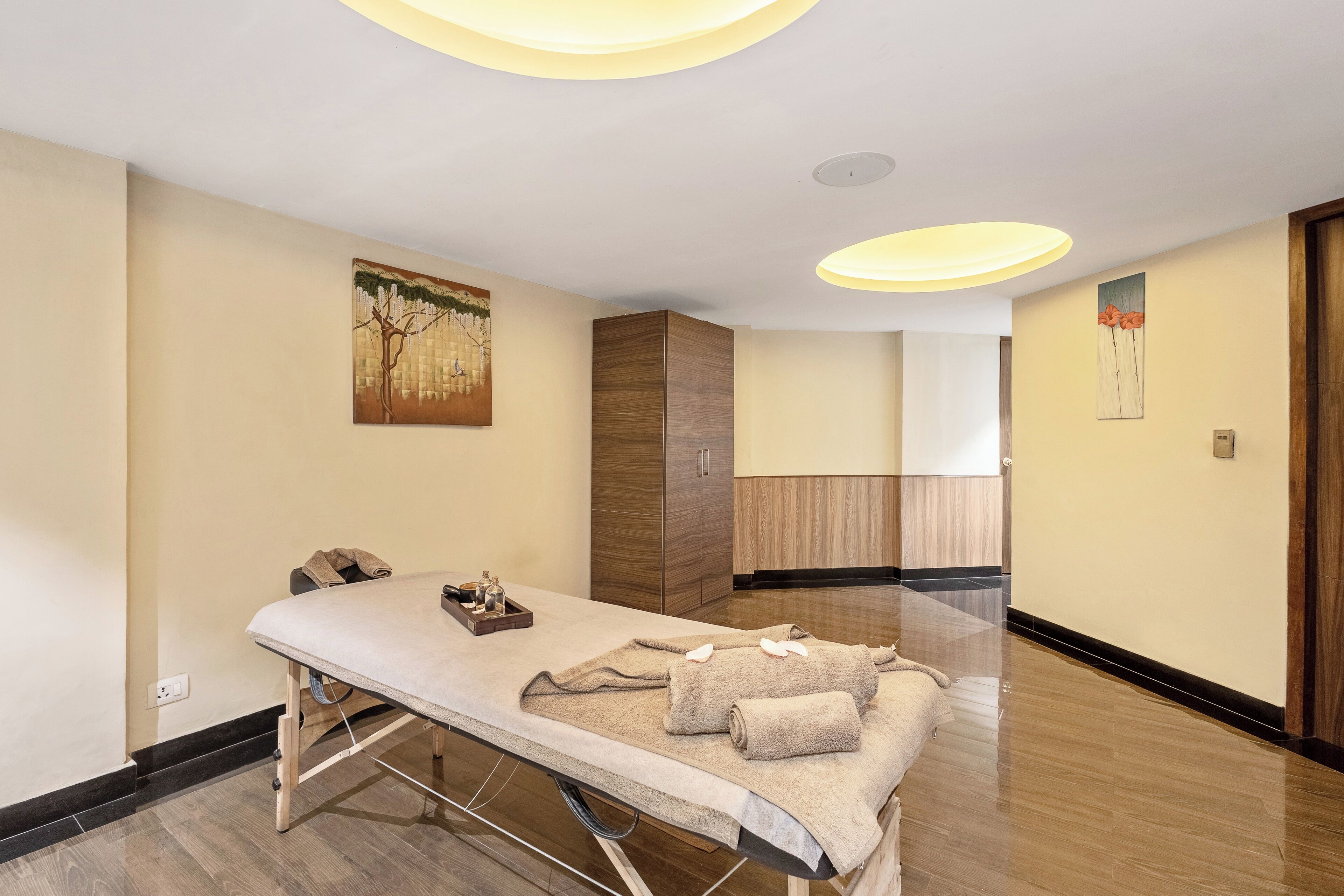 A clean, modern room with a massage table, wooden cabinets, and artwork on the walls.