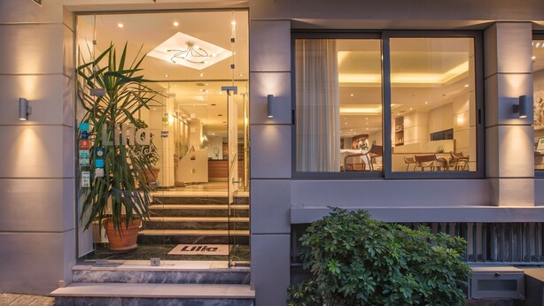 Una entrada de hotel moderna con puerta de cristal, una planta en maceta y un interior bien iluminado visible a través de la puerta.
